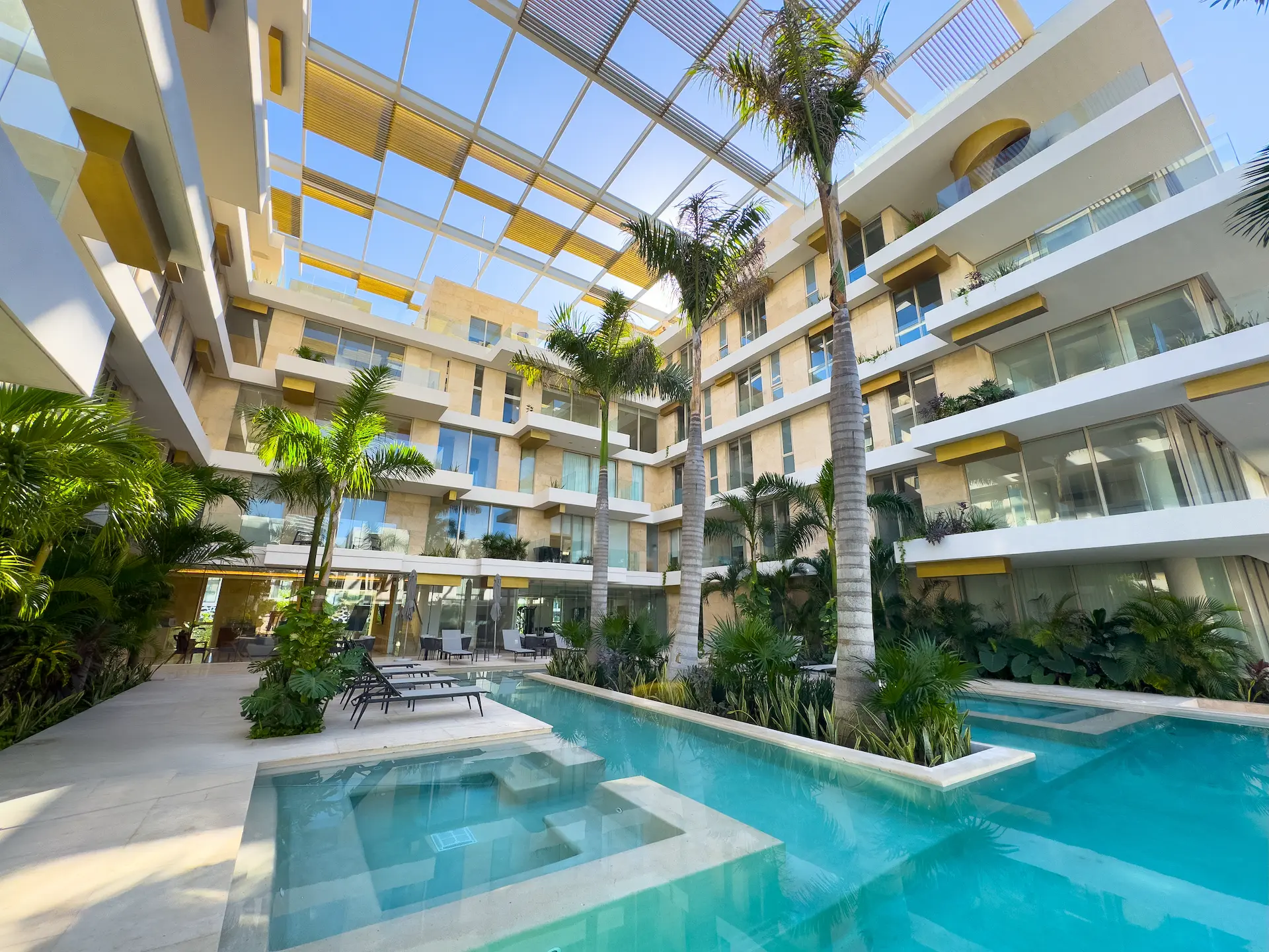 Alberca y atrio interior de Alba Marina Puerto Cancún rodeado de palmeras y jardines tropicales