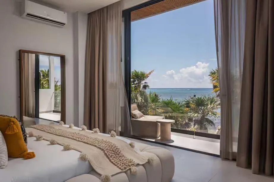 Recámara con ventanal a una terraza con vista al mar y palmeras, en Palacio del Mar