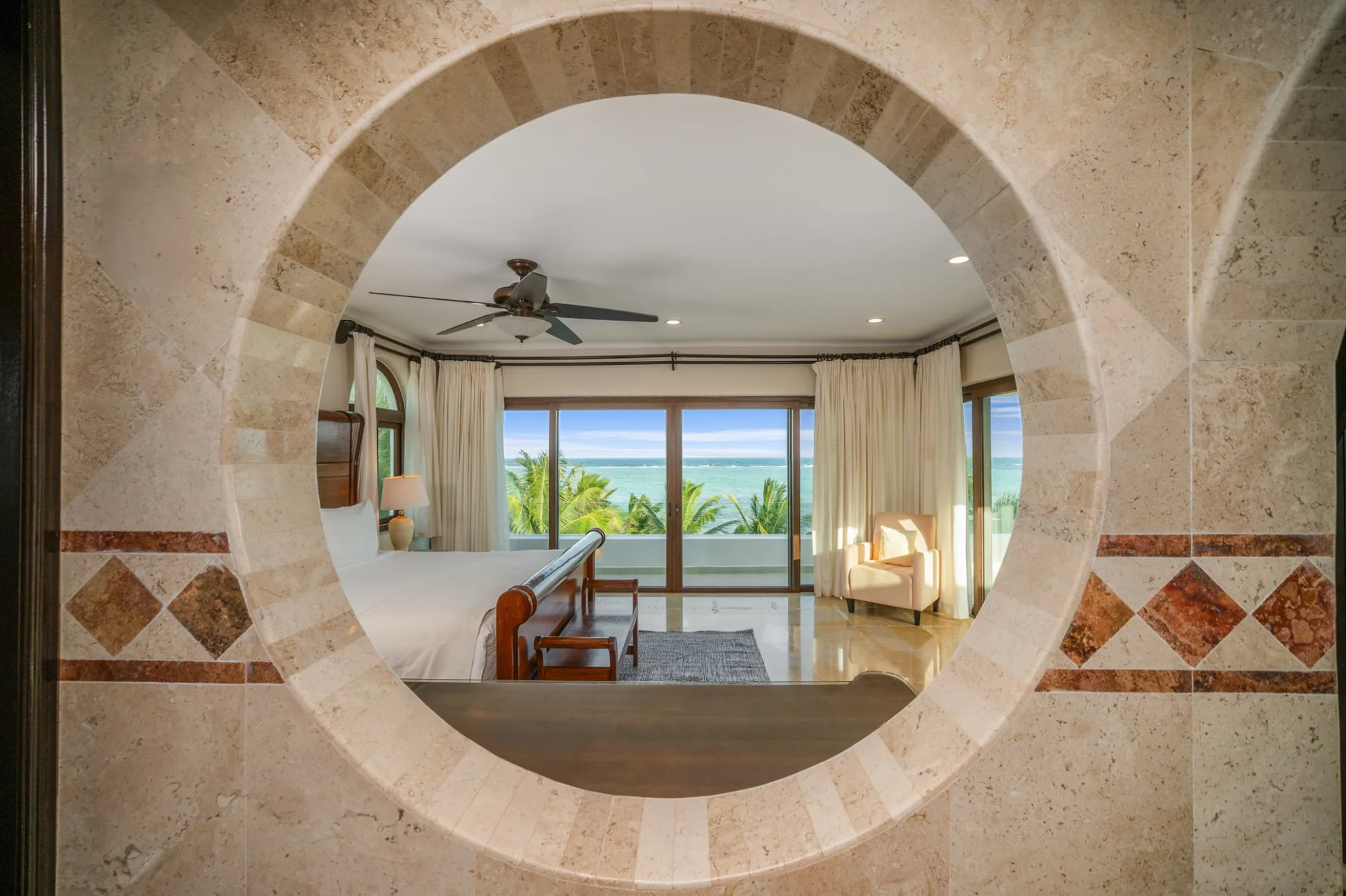 Baño de travertino con ventana circular y vista al mar en Sueño del Mar, Tulum